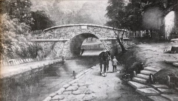 A black and white illustration of the Croydon Canal in the early 19th century. A small stone bridge goes over the canal, and a couple of people are walking alongside it.